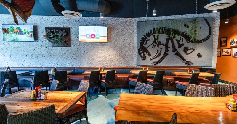 Interior with a dinosaur skeleton relief on the wall, woven chairs, wooden tables, and two televisions
