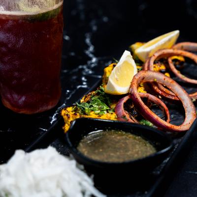 Grilled kebabs with lemon wedges on a dark table, accompanied with a red drink.