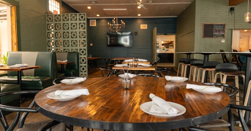 Interior of a restaurant featuring a large round wooden table set with white plates and napkins