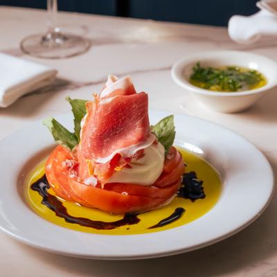 Burrata appetizer plated with tomato slices, olive oil, and balsamic drizzle.