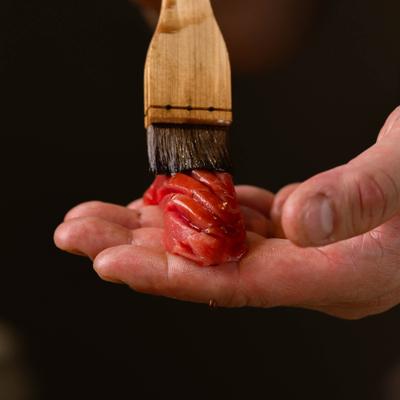 Chef applying sauce to raw tuna with a brush.