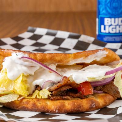 Gyro pita sandwich with seasoned meat, tzatziki, lettuce, and red onion.