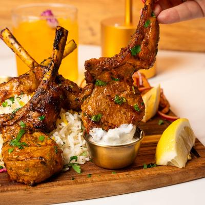 Grilled lamb chops served with rice, dipping sauce, and lemon wedges.