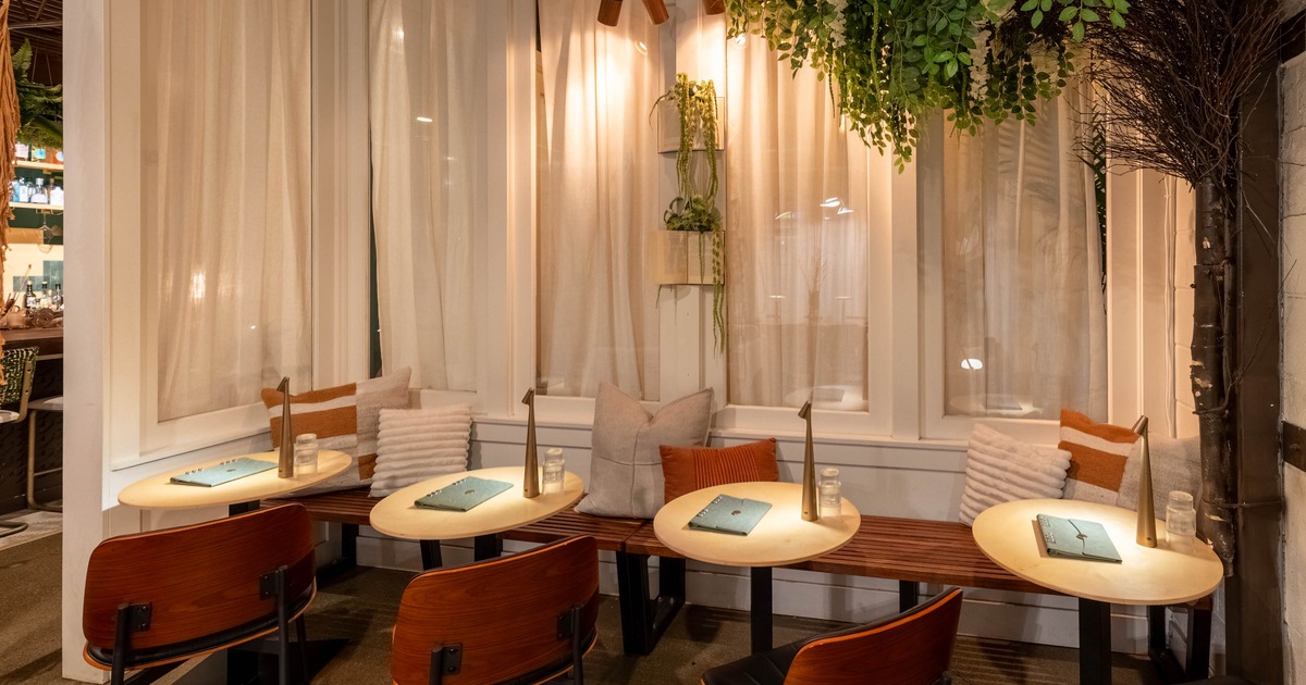 Cozy dining area with small wooden tables, wooden chairs, cushioned bench, and greenery