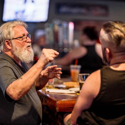 A person gesturing while in conversation with another individual in a casual, bar setting.
