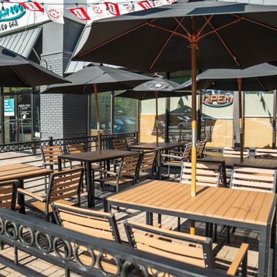 Outdoor patio with wooden tables, black umbrellas, and a metal fence.