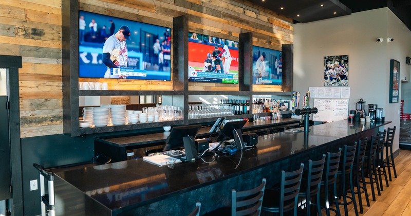 Interior of a sports bar with three televisions showing baseball, a wood plank wall