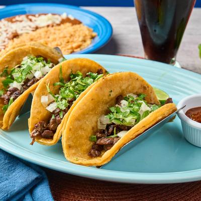 Three beef tacos topped with onions and cilantro, served with rice, beans, and salsa.