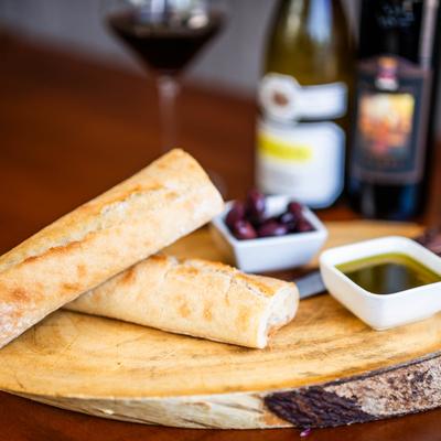 A rustic style serving of bread on a wooden board with olives, olive oil, and wine.