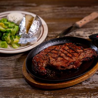 Rib eye served with broccoli, a baked potato, and dressing.