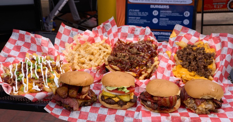 Assorted burgers and loaded fries in baskets with red-checkered paper
