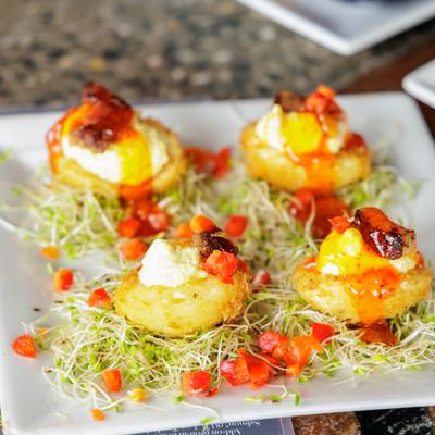 Four appetizers on a square plate with sprouts, topped with cream, red peppers and orange sauce.