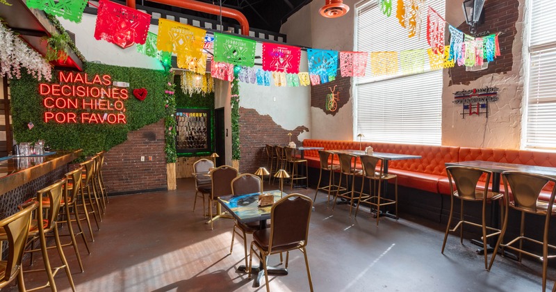 Vibrant restaurant interior with colorful papel picado, neon sign, and orange seating