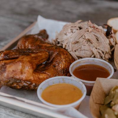 Half chicken and pulled pork served on a tray with sauces and sides.