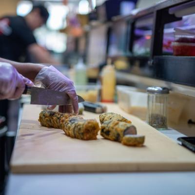 Chef slicing a freshly deep-fried sushi roll on a wooden cutting board.