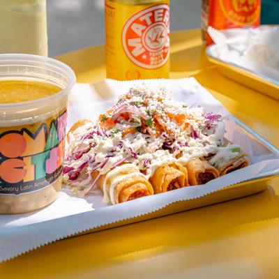 Flautas topped with green garlic sauce, cream, cabbage, tomato, and cheese.