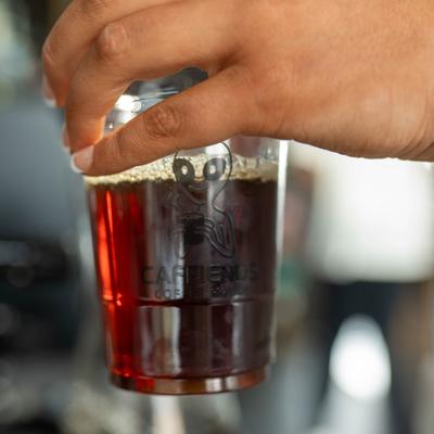 Hand holding a cup of iced coffee with foam.