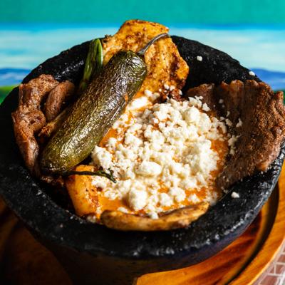 Molcajete bowl with chicken, steak, shrimp, chorizo, salsa, scallions, jalapenos, and cheese.