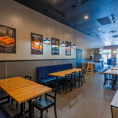 Interior of a modern cafe with wooden tables, black chairs, blue upholstered bench, and food posters on beige walls.
