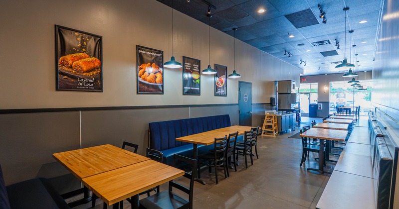 Interior of a modern cafe with wooden tables, black chairs, blue upholstered bench, and food posters on beige walls
