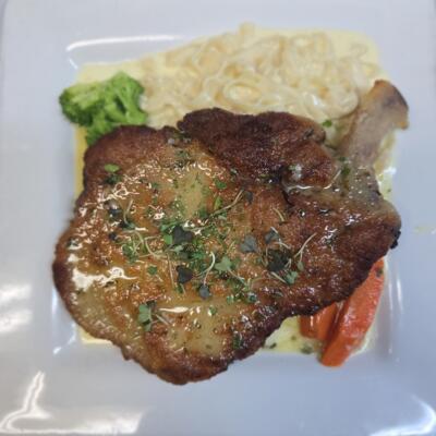 French Cut Pork Chop, Pounded Lightly Breaded Topped With a Lemon Butter Sauce Served With Fettuccine Alfredo Sauce.