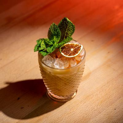 Mai Tai in a textured glass with ice, mint leaves, and dry lime wheel, set on a wooden table.