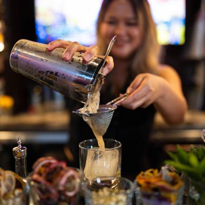 A bartender straining a cocktail into a glass.