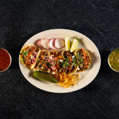 Street tacos served with grilled onions, jalapeno, radish slices, lemon wedges and dips.