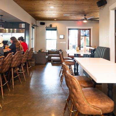 Brown leather bar stools and tables, a ceiling fan, and customers seated at the bar.