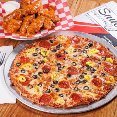 A pepperoni pizza, chicken wing plate, a menu, and seasoning shakers on a wooden table.