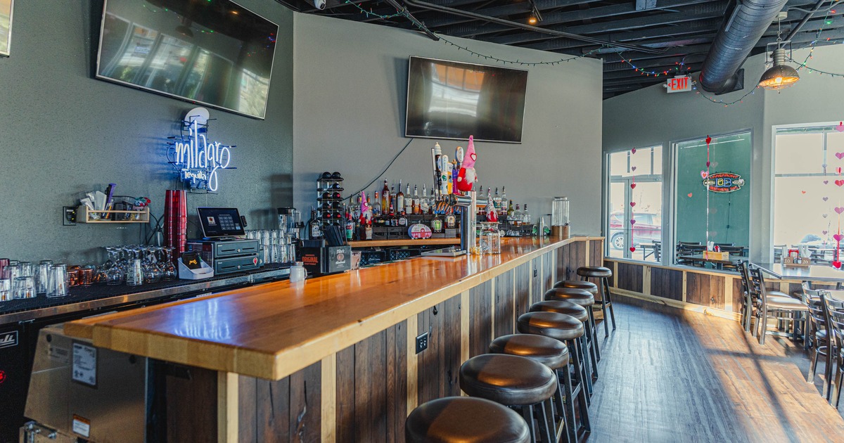 Bar area with a wooden counter, stools and TV screens on the wall