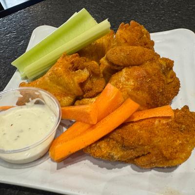 Crispy chicken wings with carrots, celery, and ranch dip on a white plate.