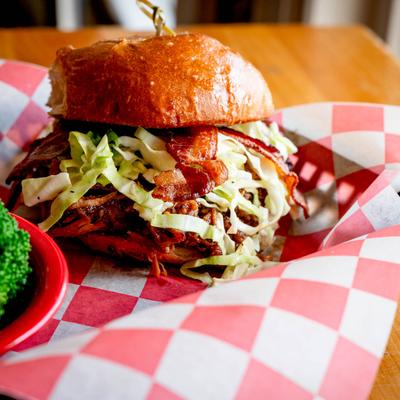 Pulled pork sandwich with bacon and coleslaw served with broccoli.
