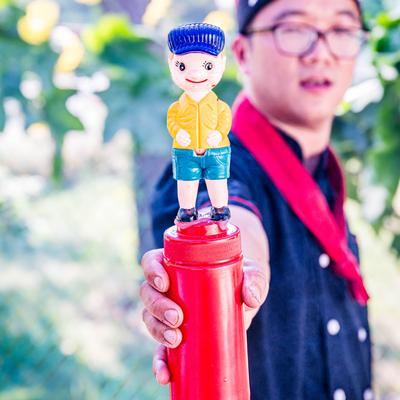 Chef holding a red bottle with a miniature figure on top.