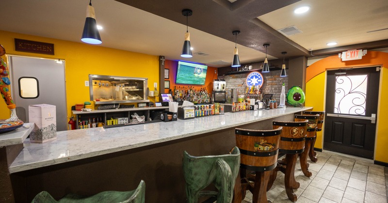 Inside a restaurant bar with a marble-topped counter, wooden chairs, and pendant lights