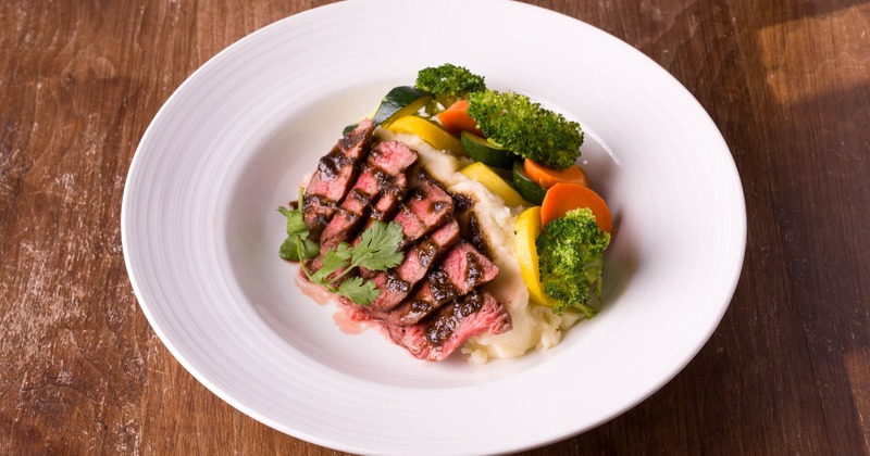 Flank steak served over mashed potatoes with vegetables on the side