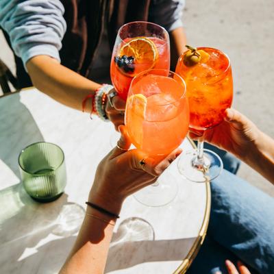 Three people toast with orange cocktails at an outdoor table.