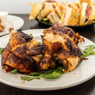 Rotisserie chicken over mixed greens with a platter of sandwiches in the background.