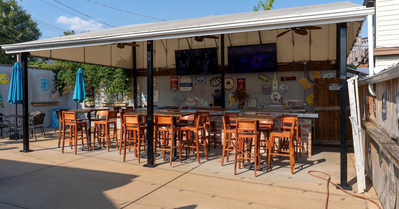 Covered outdoor patio with high top tables, TVs, and bar seating