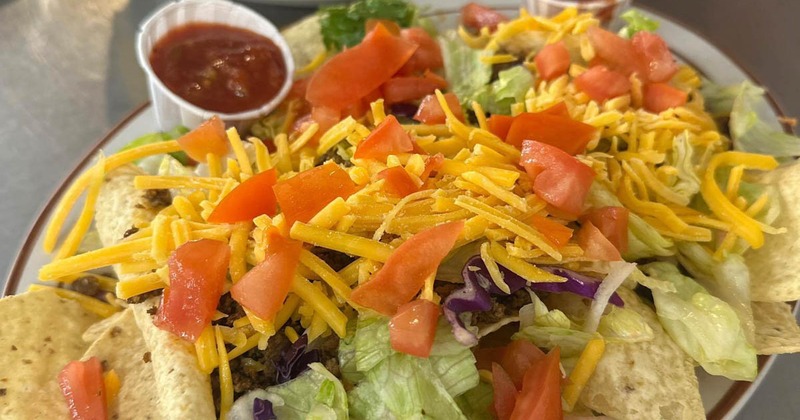 Loaded nachos with lettuce, tomatoes, cheese, and two cups of salsa