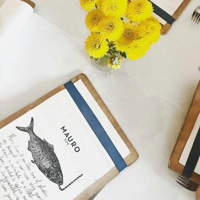 Restaurant menu beside a bouquet of yellow flowers on a white tablecloth.