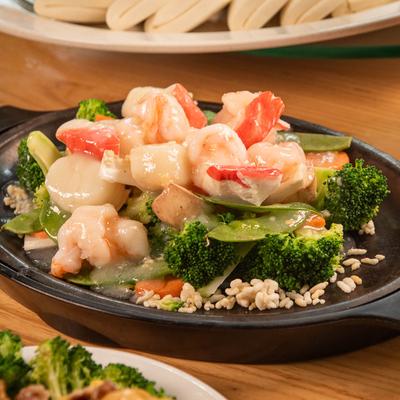 Sizzling seafood stir-fry on a black platter with broccoli, shrimp, and vegetables.