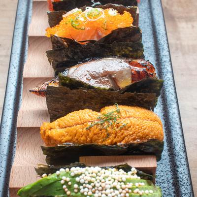 Assorted sushi pieces with various toppings arranged in a wooden and black tray.