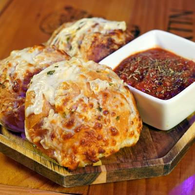 Cheesy garlic Knots served on a wooden board with marinara dip.