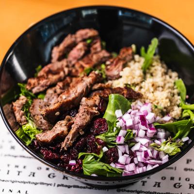 Beef salad bowl with quinoa, greens, dried cranberries, and diced onions.