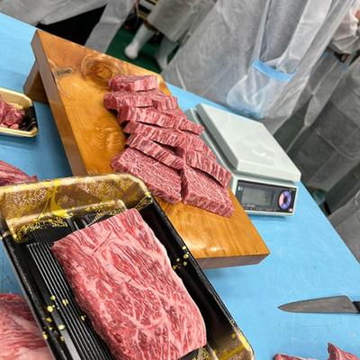 Sliced marbled meat on a wooden board and tray, with a digital scale on a blue table.