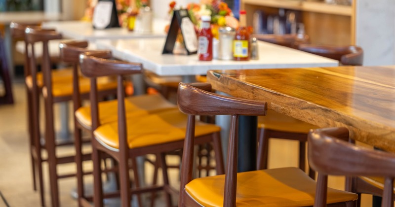 Wooden chairs with yellow cushions around a wooden table in a restaurant.