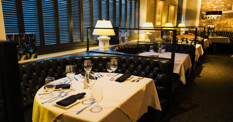 Tufted black leather booths with tables set with wine glasses, and illuminated partition lamps
