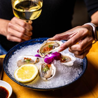 A person holding an oyster over a bowl of ice with lemon and wine.