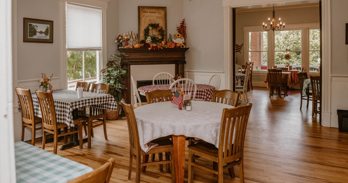 A cozy dining room with wooden floors, tables with tablecloths and wooden chairs